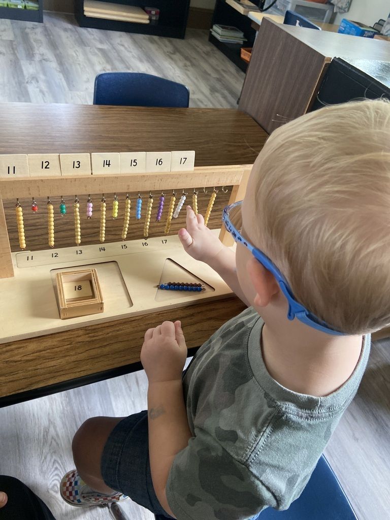 Child using a wooden learning activity board with hanging beads in a classroom setting