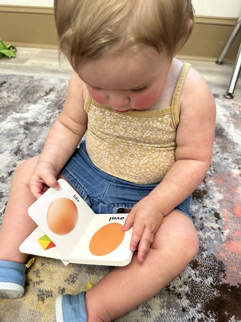 Toddler sitting on a rug, looking at a shape puzzle with orange pieces.