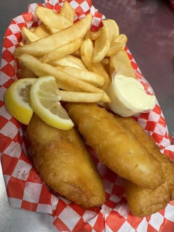 Fish and chips in red checkered basket, with lemon slices and dipping sauce.
