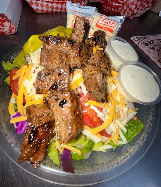 Steak salad with cheese, tomatoes, and dressing in a clear bowl with crackers.