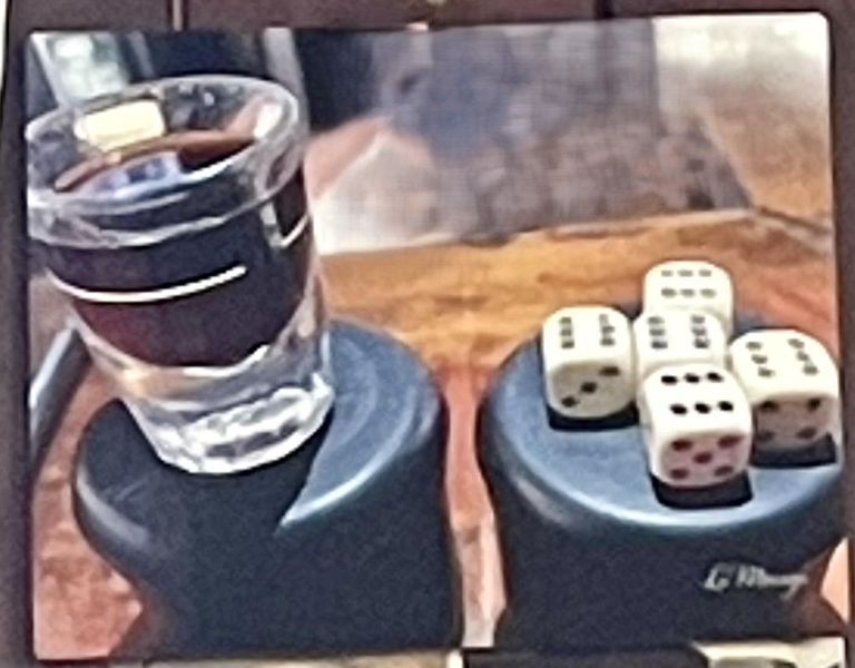 Shot glass of dark liquid beside a dice cup with five dice showing various numbers.