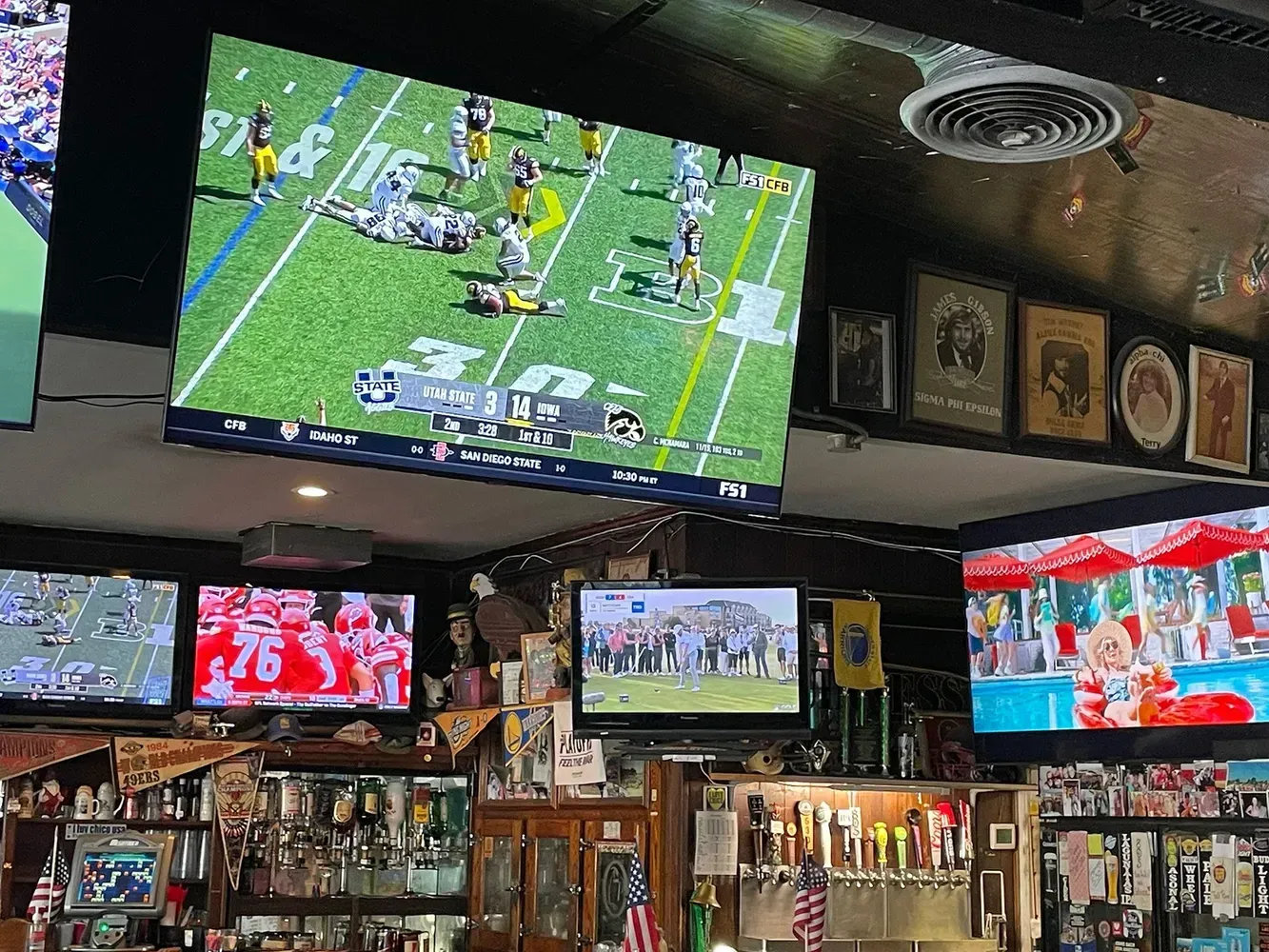 Televisions in a bar showing football and festive content. Bottles and beer taps are also visible.