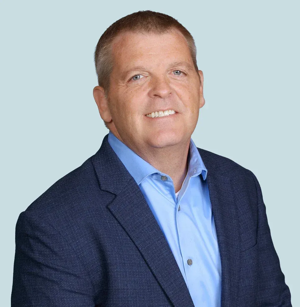 Smiling man in a navy blazer and light blue shirt against a pale blue background