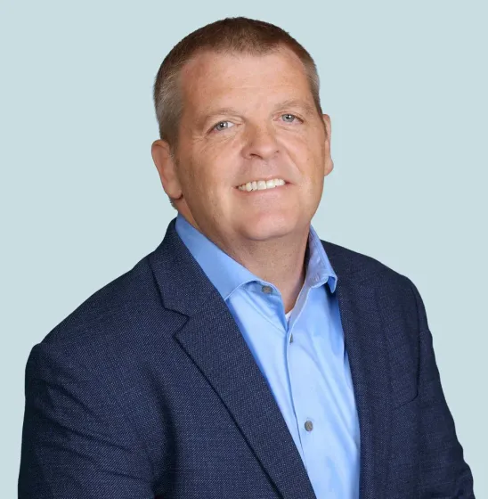 Smiling man in a navy blazer and light blue shirt against a pale blue background