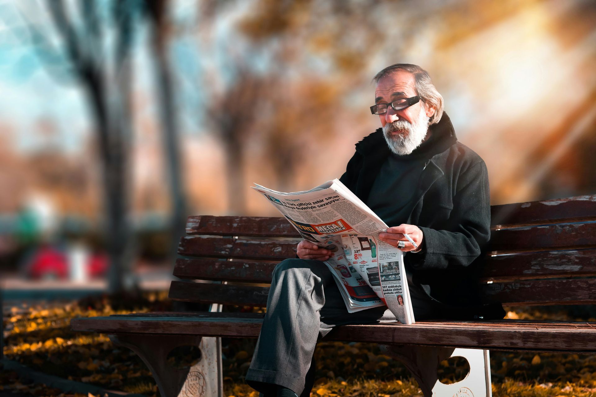 Un homme âgé est assis sur un banc de parc et lit un journal.