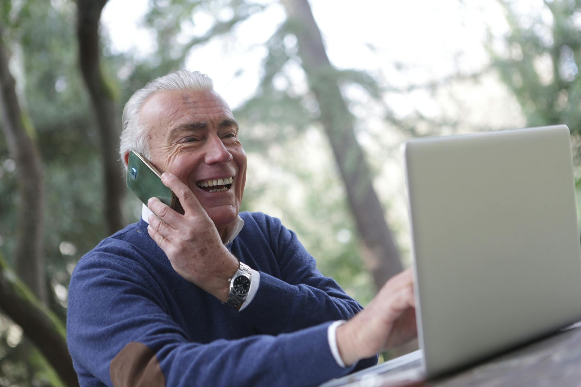 Un homme âgé parle au téléphone portable tout en utilisant un ordinateur portable.