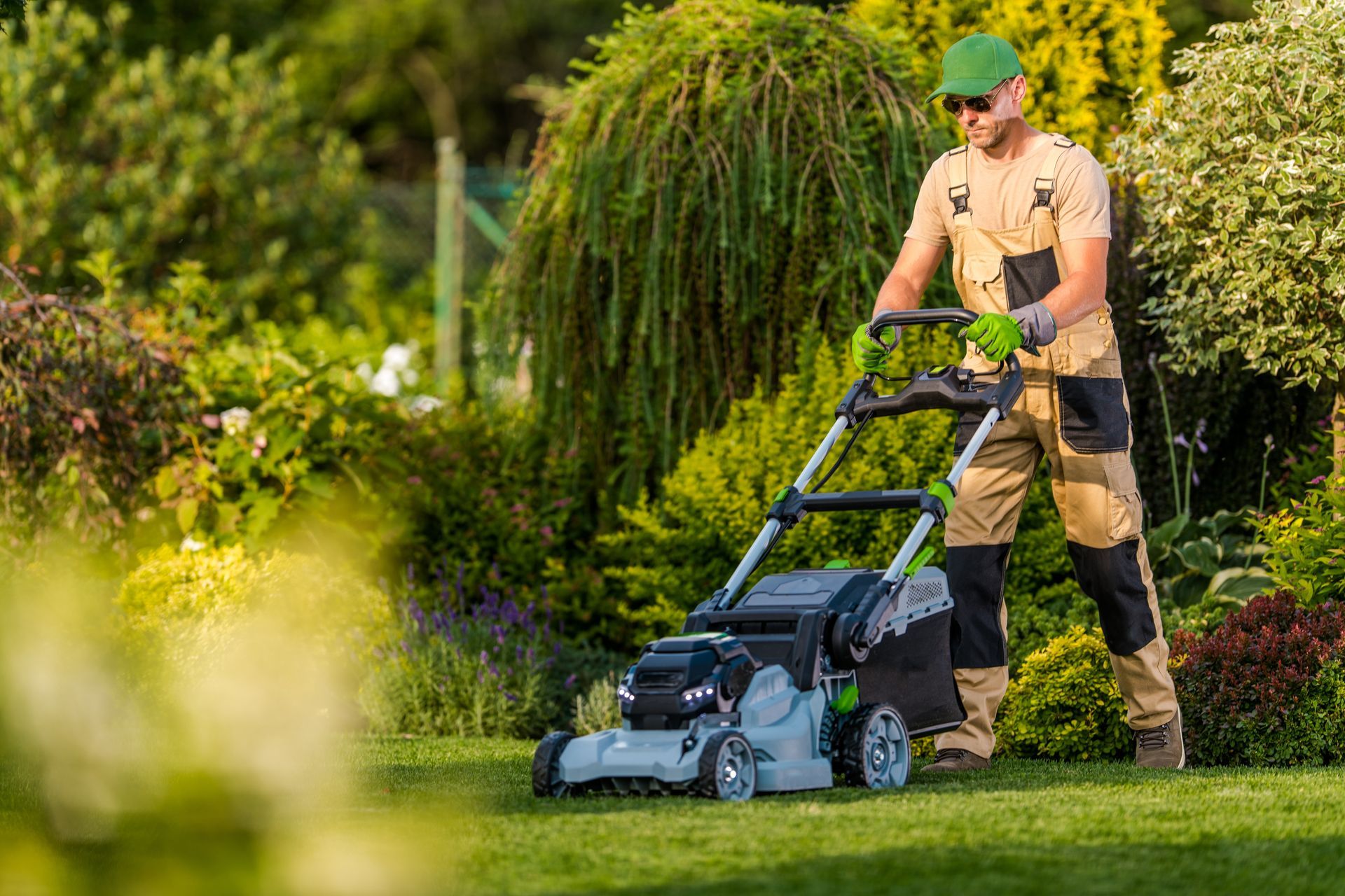 Man mowing a green lawn with an electric lawnmower in a garden setting.