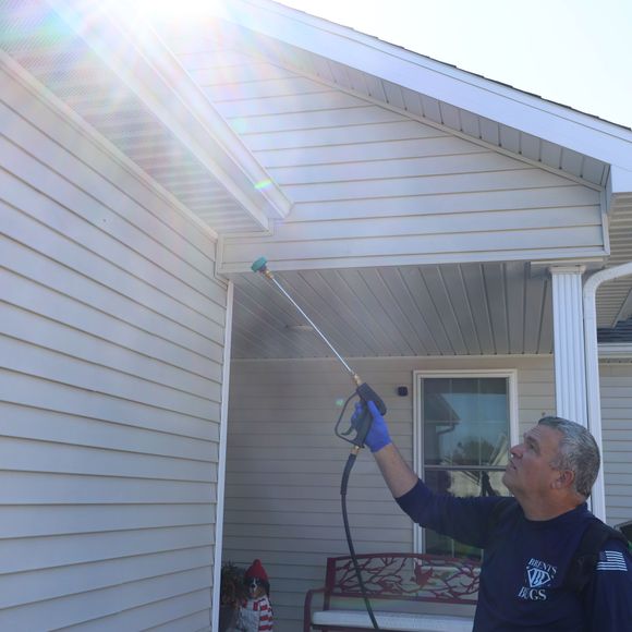 Person pressure-washes white house siding under a bright sun flare