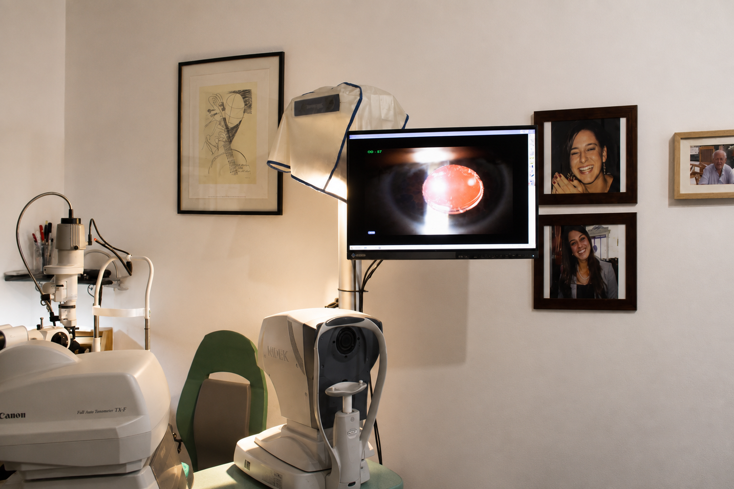 Sala per esami oculistici con attrezzature, ritratti incorniciati e un monitor che mostra una scansione ravvicinata dell'occhio.