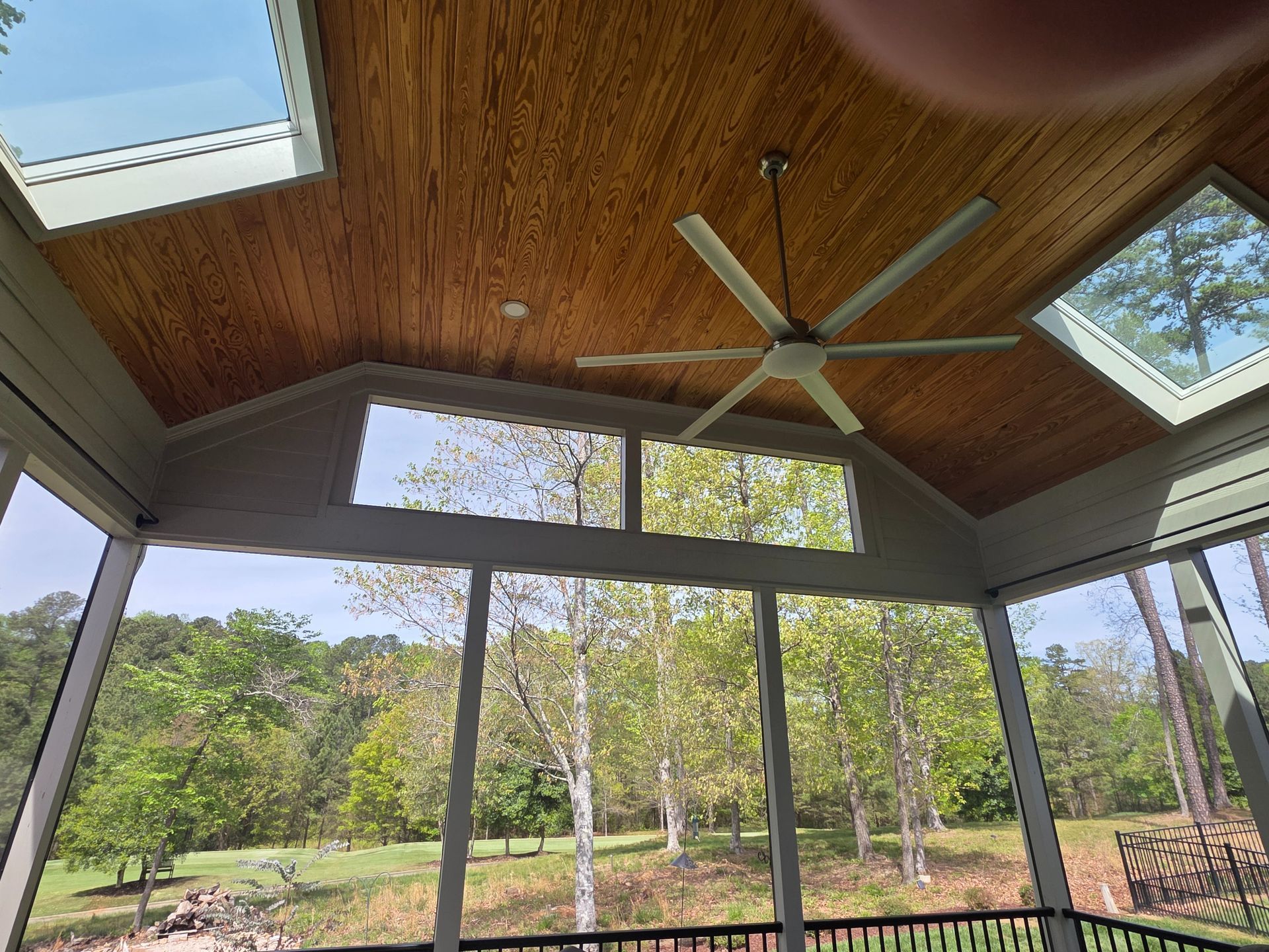 Screened porch with wood ceiling, ceiling fan, and windows overlooking a green yard and trees