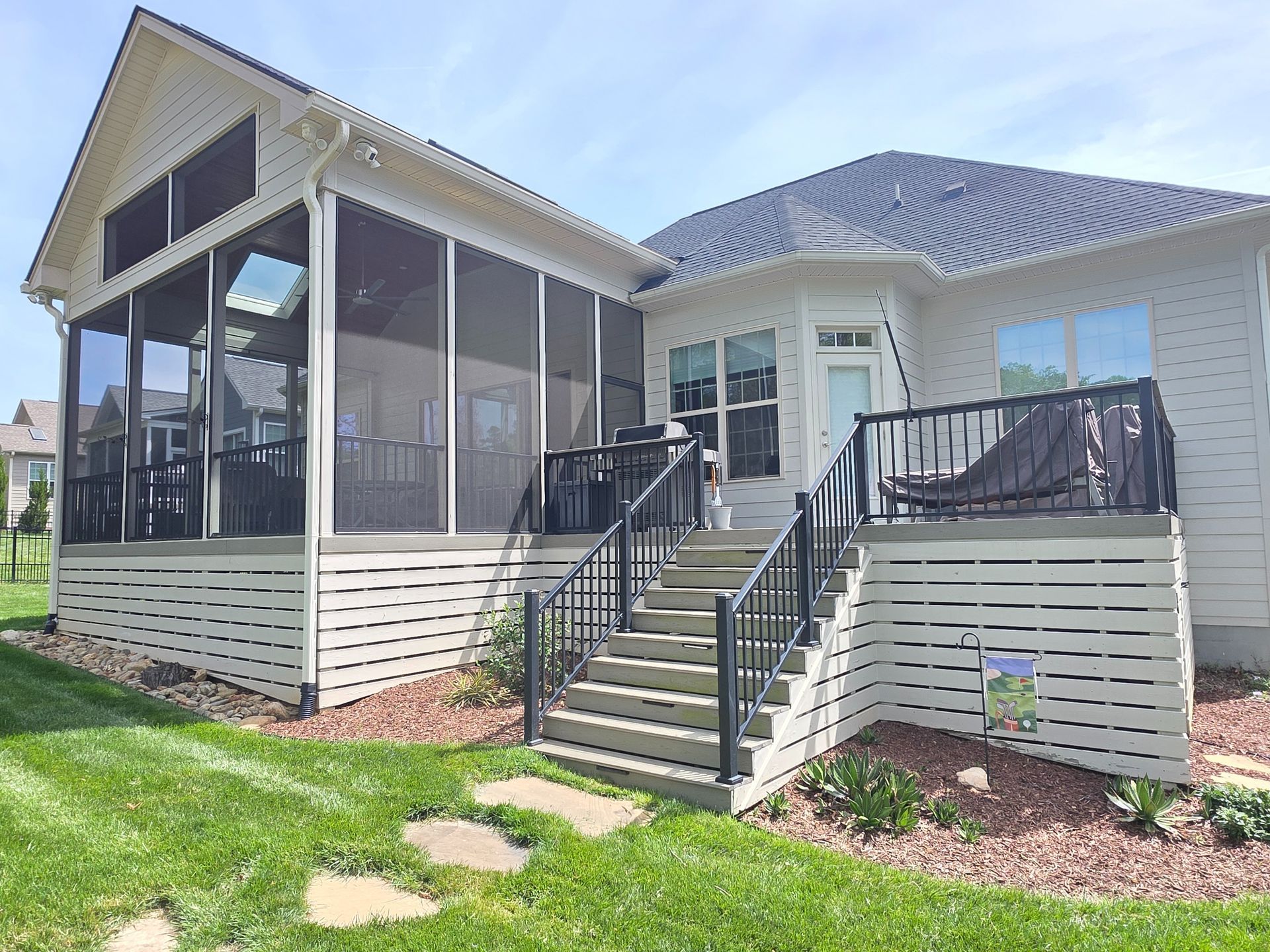 Back porch deck with stairs, screened enclosure, and black railing on a suburban house
