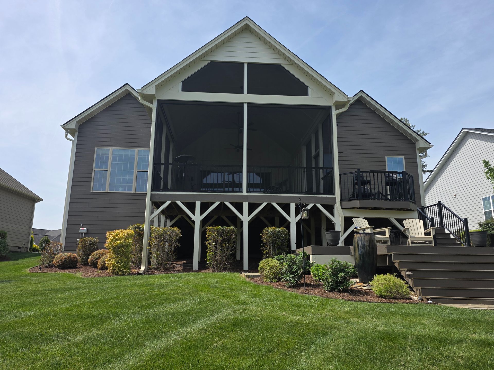 Raised gray house with front deck, stairs, and manicured lawn