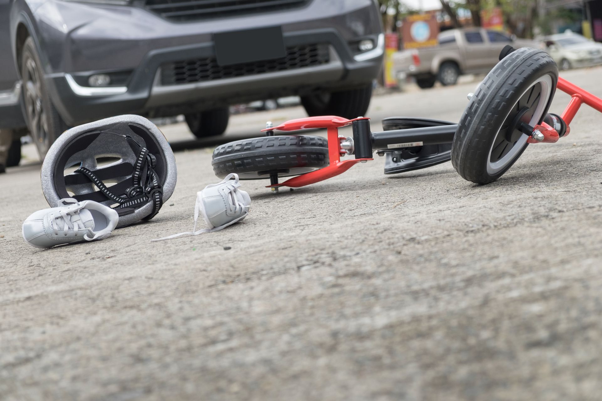 A car is near a child's tricycle and personal items on a paved road, possibly after an accident.