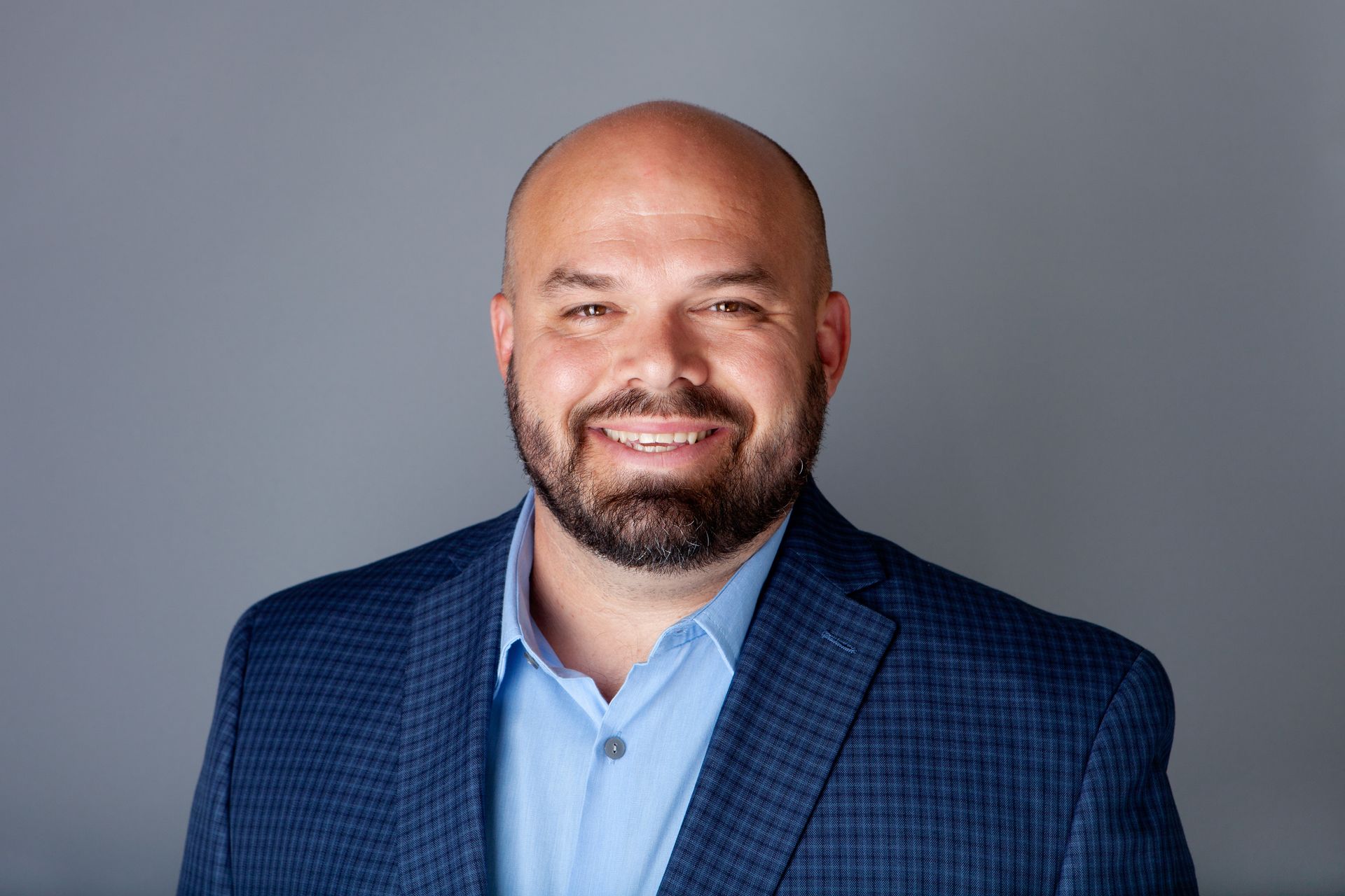 A bald man with a beard is wearing a blue suit and smiling for the camera.
