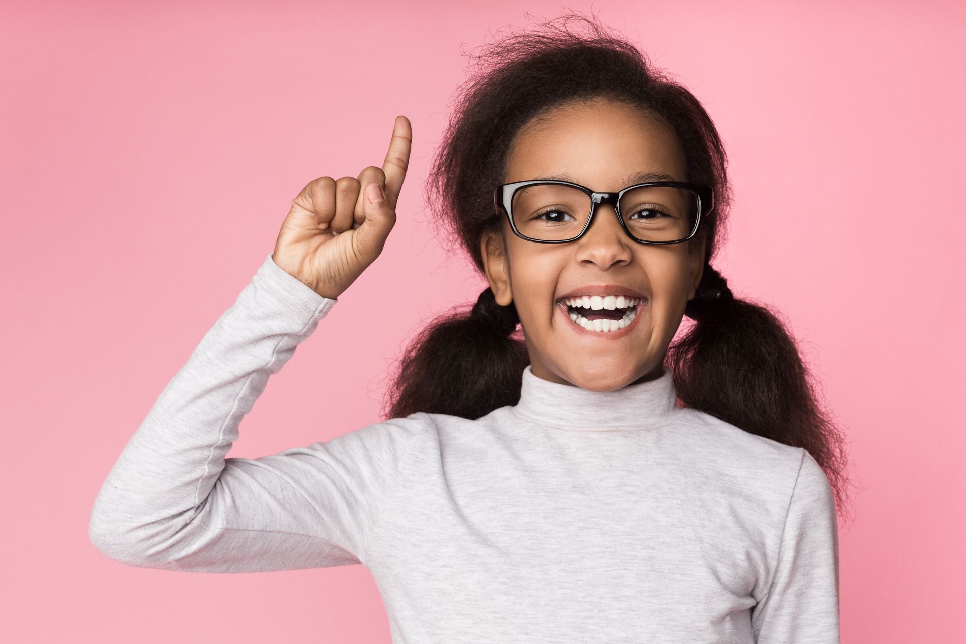A little girl wearing glasses is pointing up with her finger.