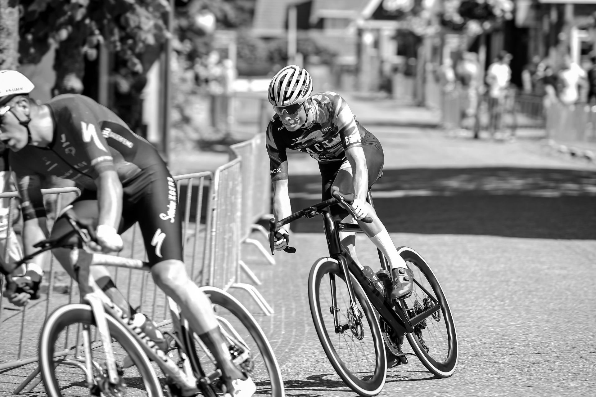Two men are racing road bicycles with carbon wheels down a street in a black and white photo.