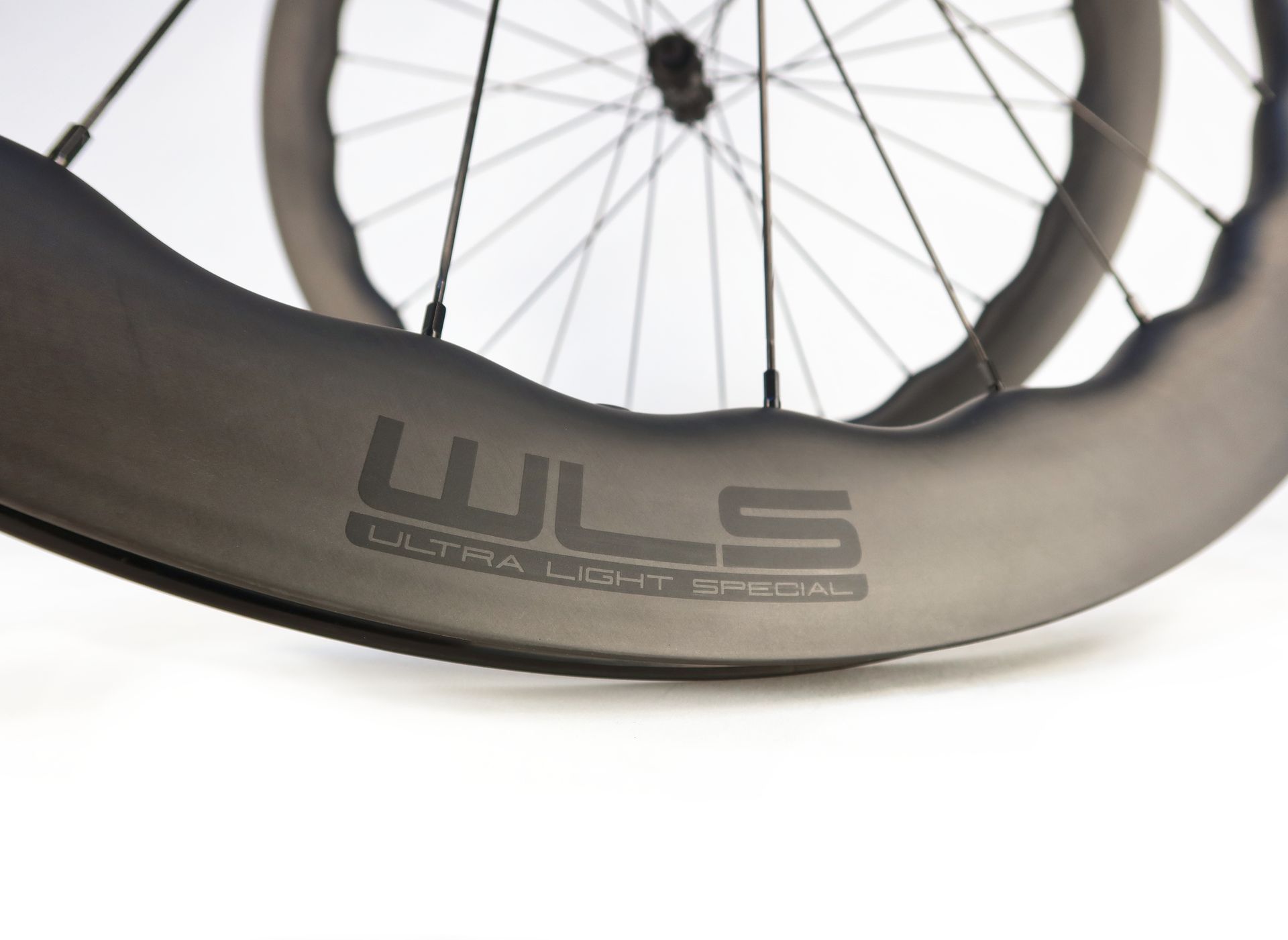 A close up of a waved carbon allroad wheel on a white background
