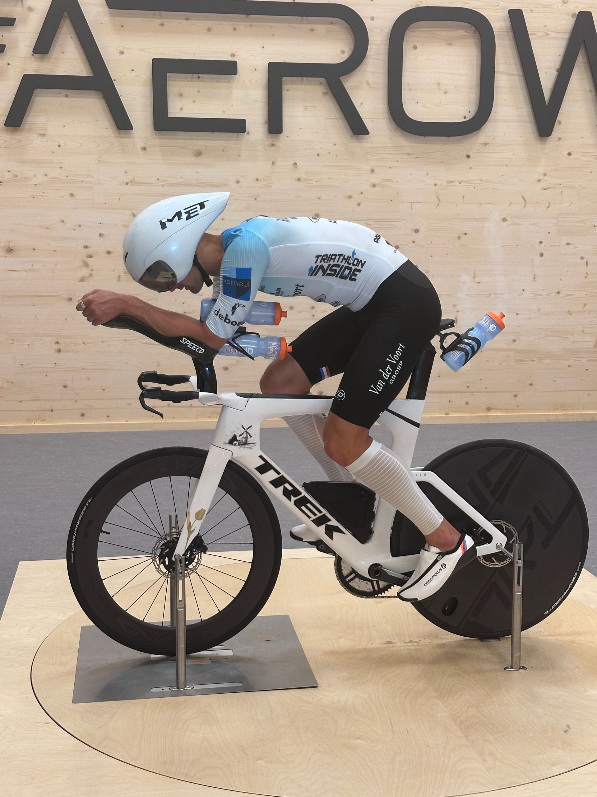 A man is riding a trek bike in front of a sign that says aerow