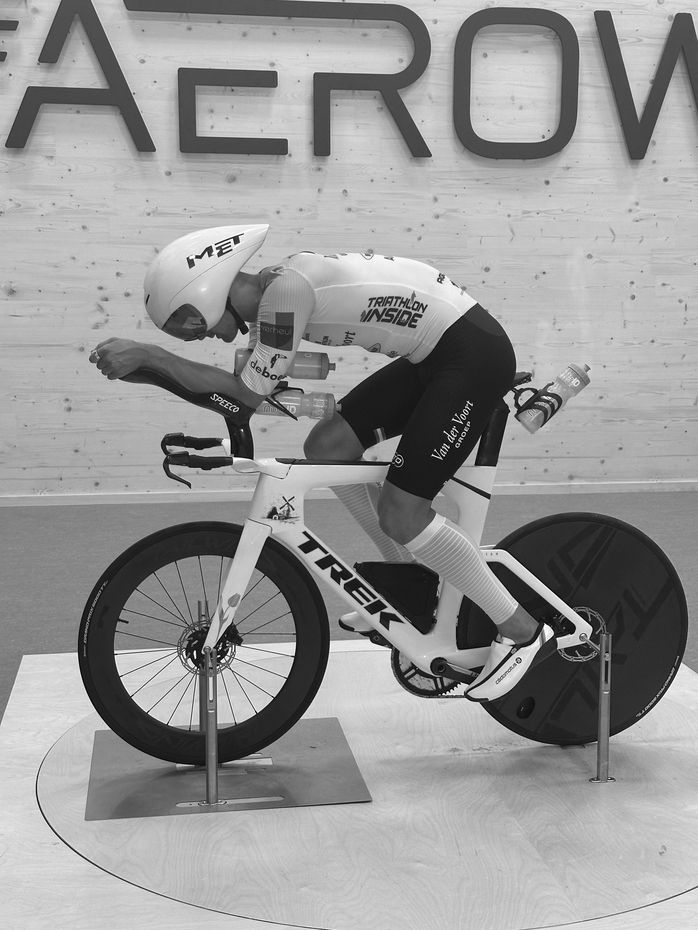 A black and white photo of a man riding a Triathlon bike  with carbon Tailwind wheels