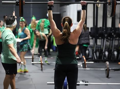 A woman is lifting a barbell over her head in a gym.