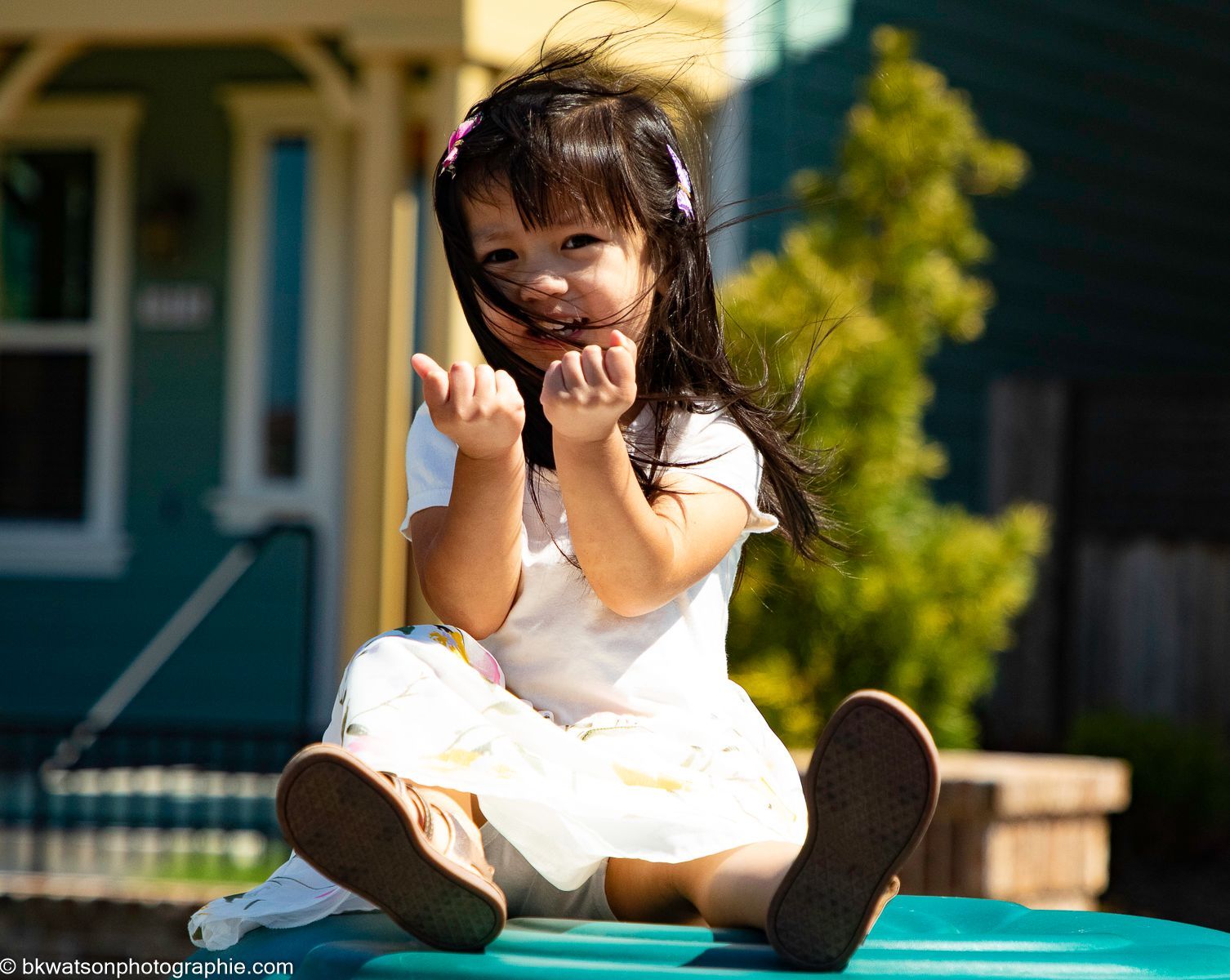 Girl with dark hair sits outside with arms up, smiling.
