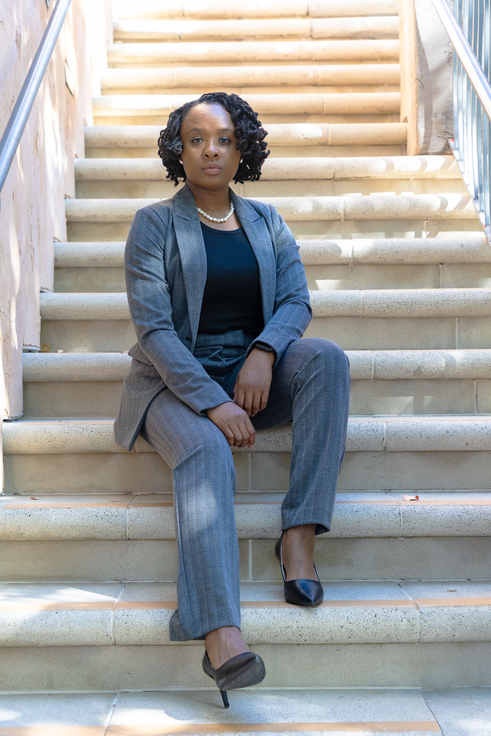 Woman in gray suit sits on outdoor stone stairs, looking at the camera.