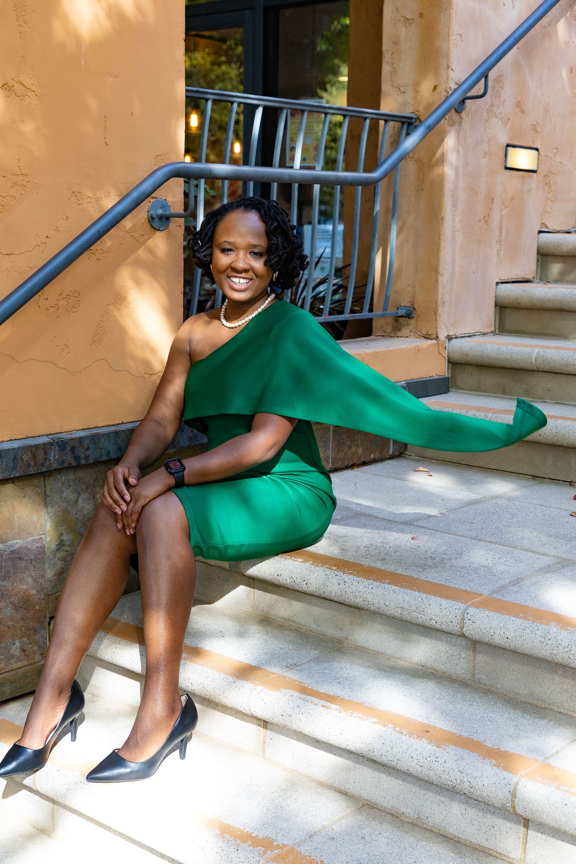 Woman in green dress, smiling, seated on outdoor steps with railing.