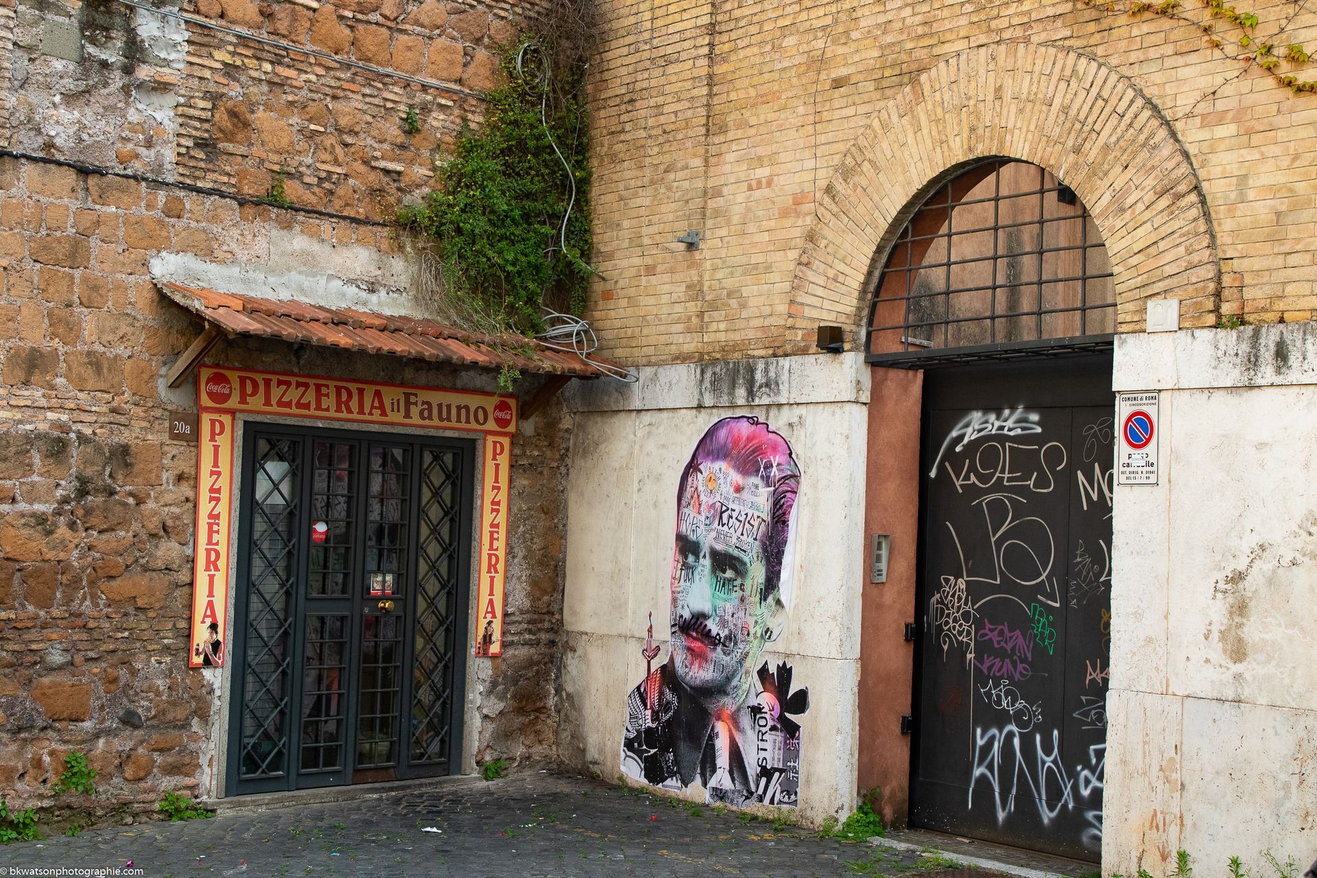 Exterior of a building with three openings: a door, a barred gate, and an arched doorway. Street art adorns the wall.