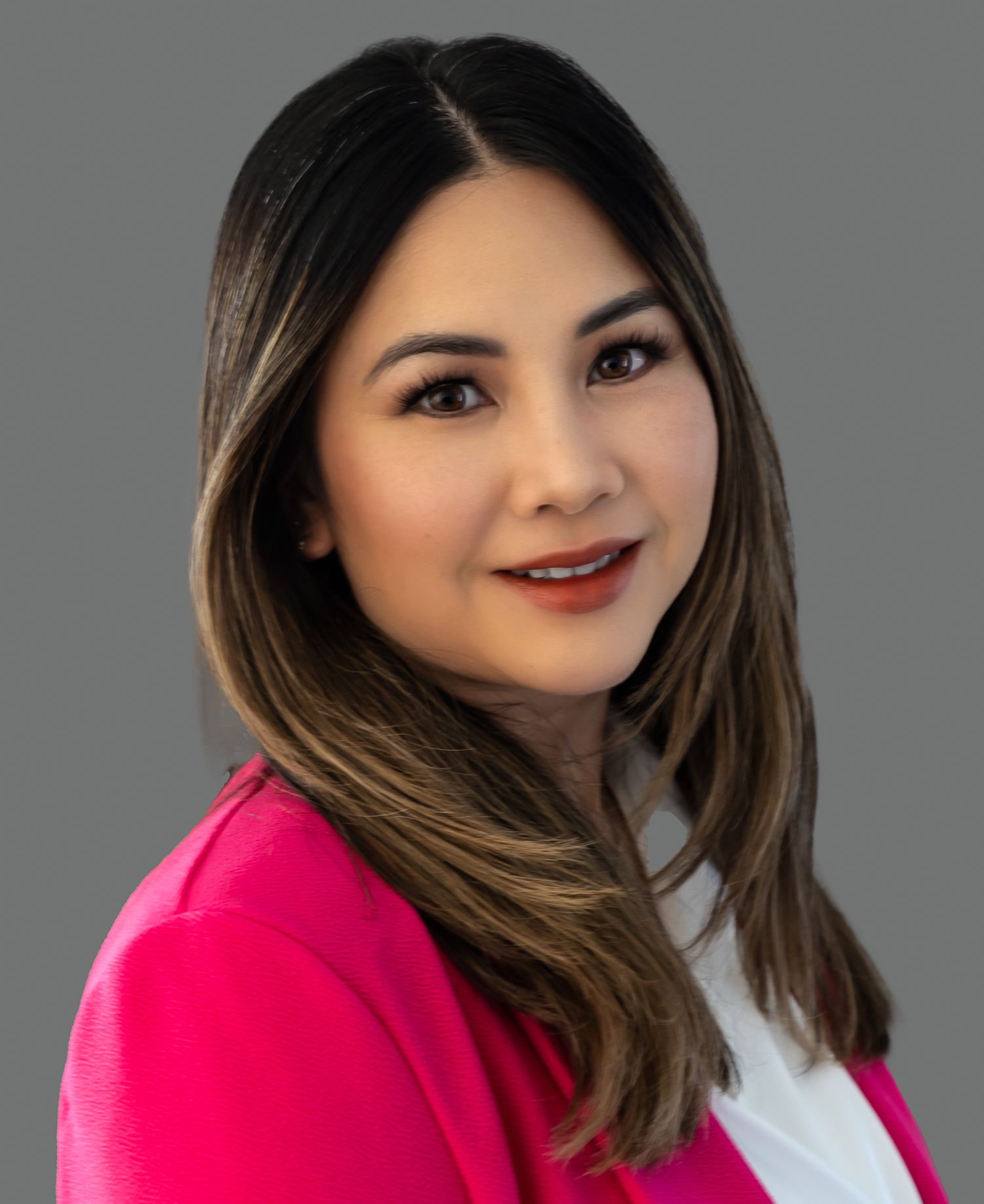 Woman in a pink blazer smiles at the camera against a gray background.