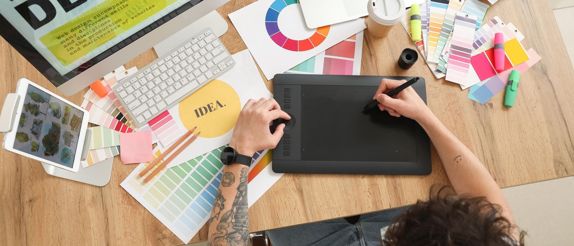 Person using a digital pen on a drawing tablet, surrounded by color palettes and design tools.
