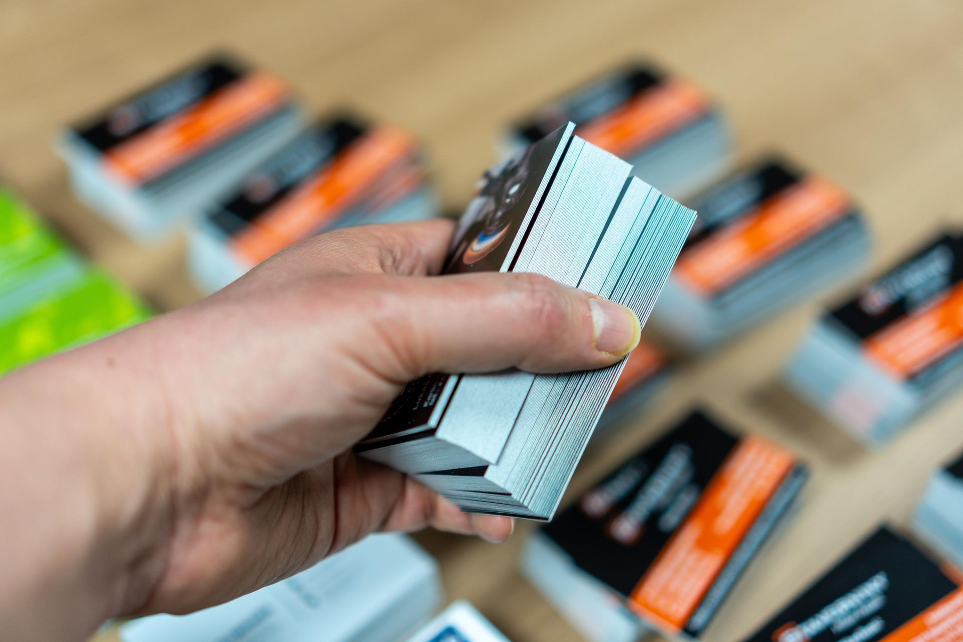 Hand holding a stack of business cards; more stacks visible in the background.