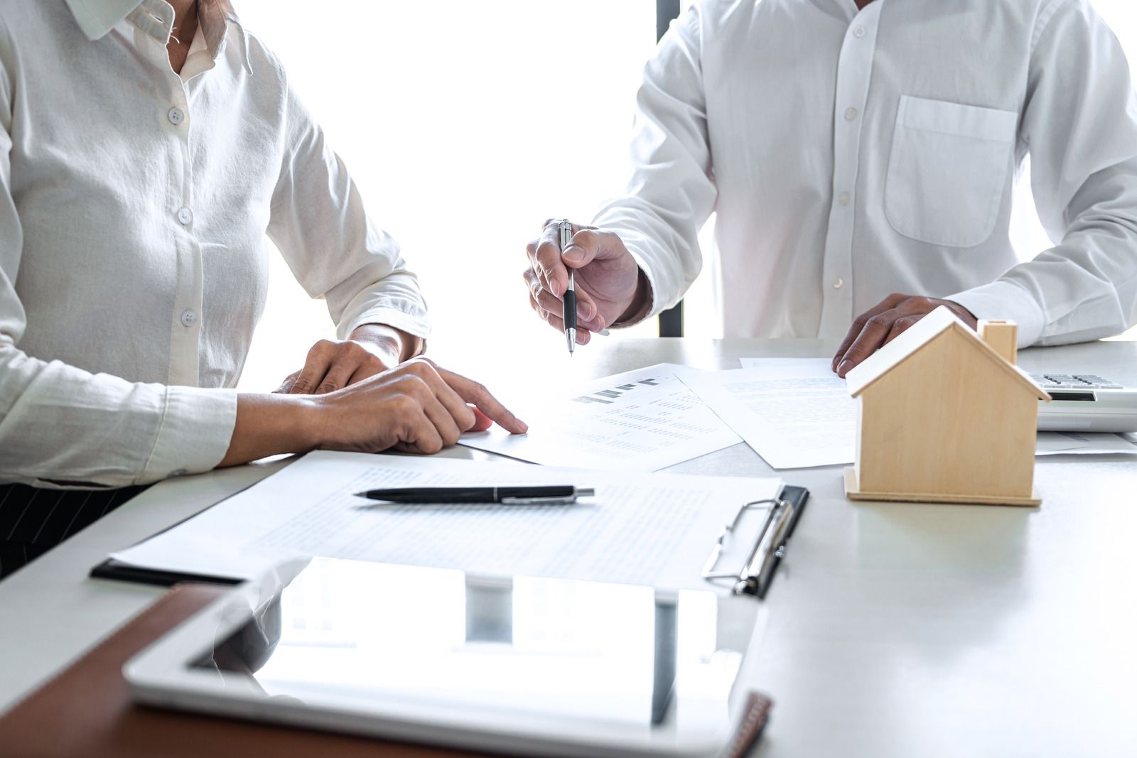 Two people reviewing documents at a table; small house model present.