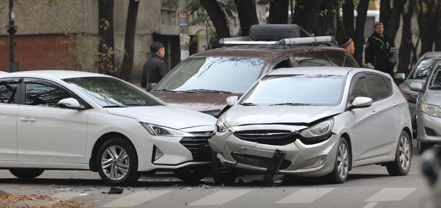 Two damaged cars, a white sedan and a silver hatchback, after a front-end collision on a city street.