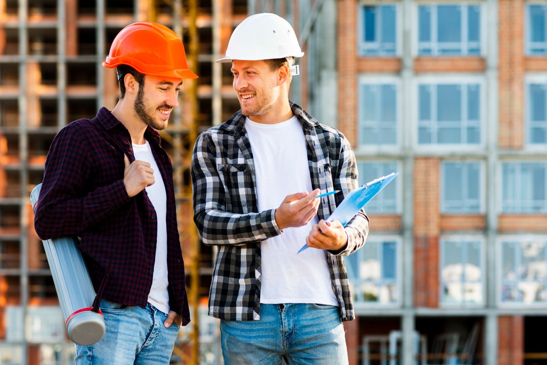 Two construction workers in hard hats reviewing blueprints outside a building