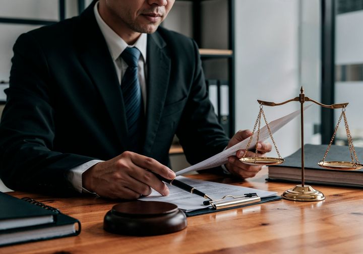 Lawyer in a dark suit reviewing documents at a desk with a gavel and scales of justice