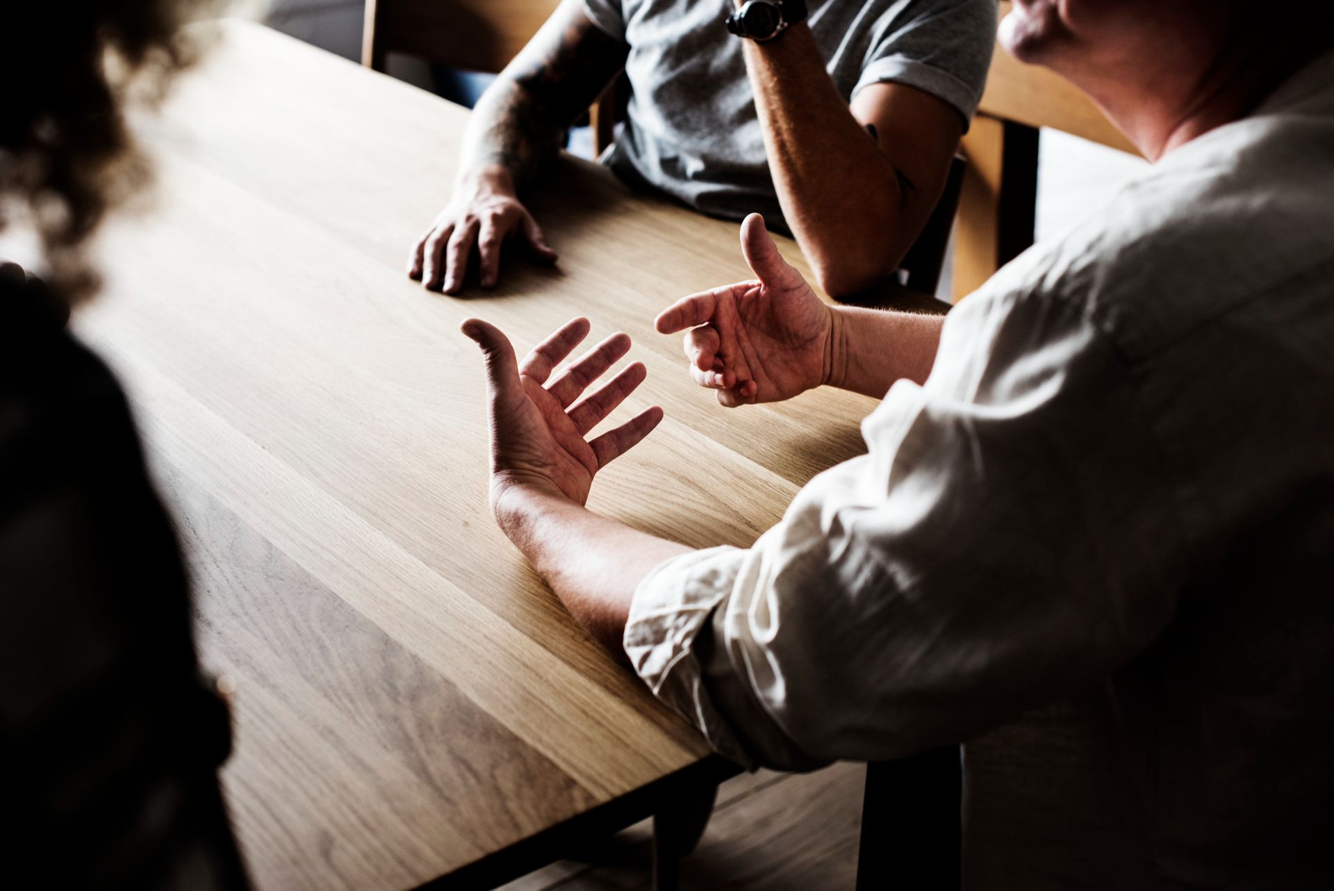 People in a meeting around a wooden table, gesturing during discussion
