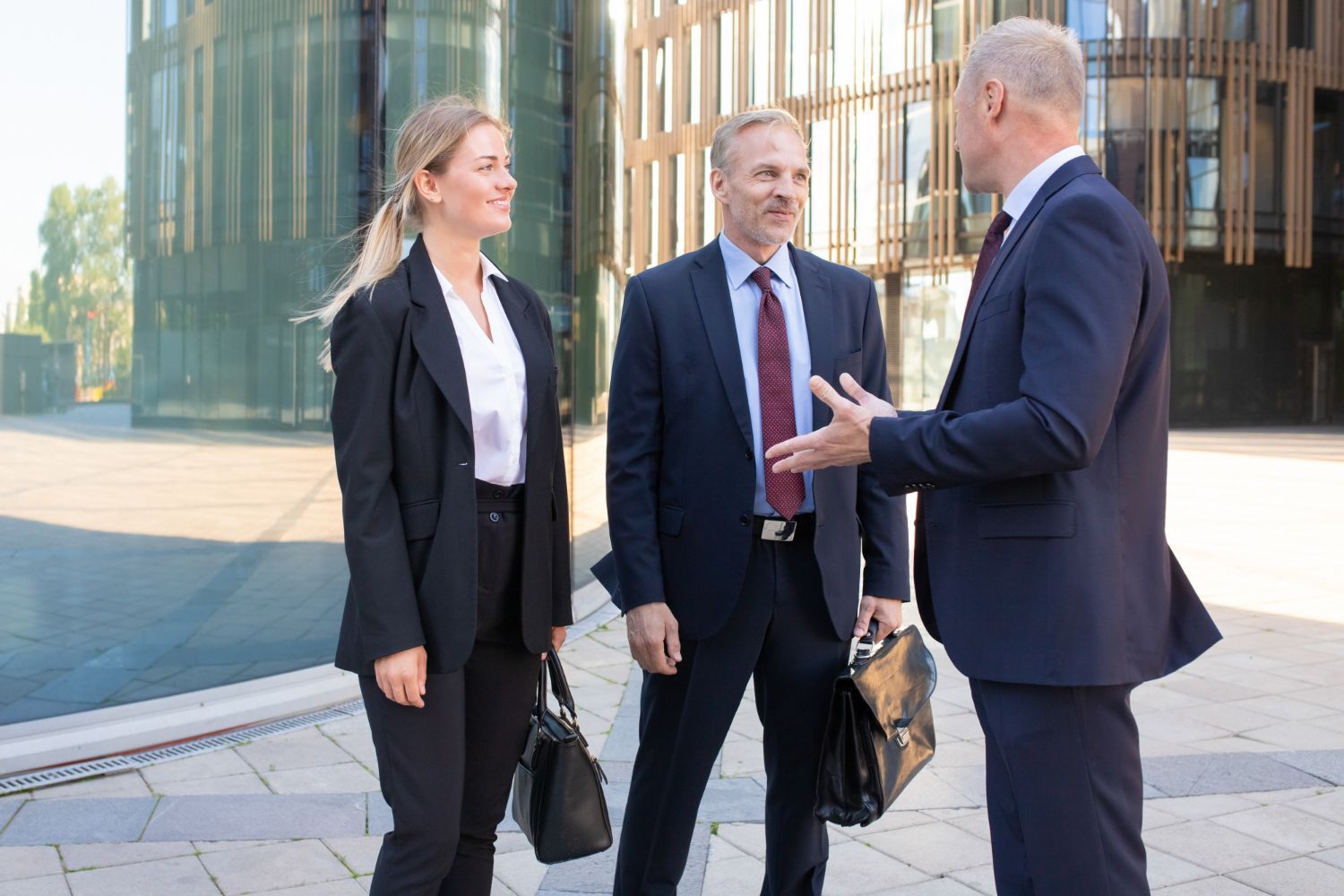 Three businesspeople talking outside a modern glass office building.