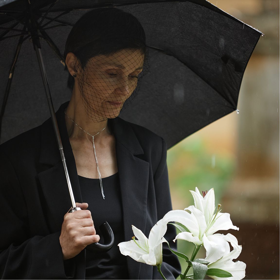 Woman under black umbrella holding white lilies in the rain