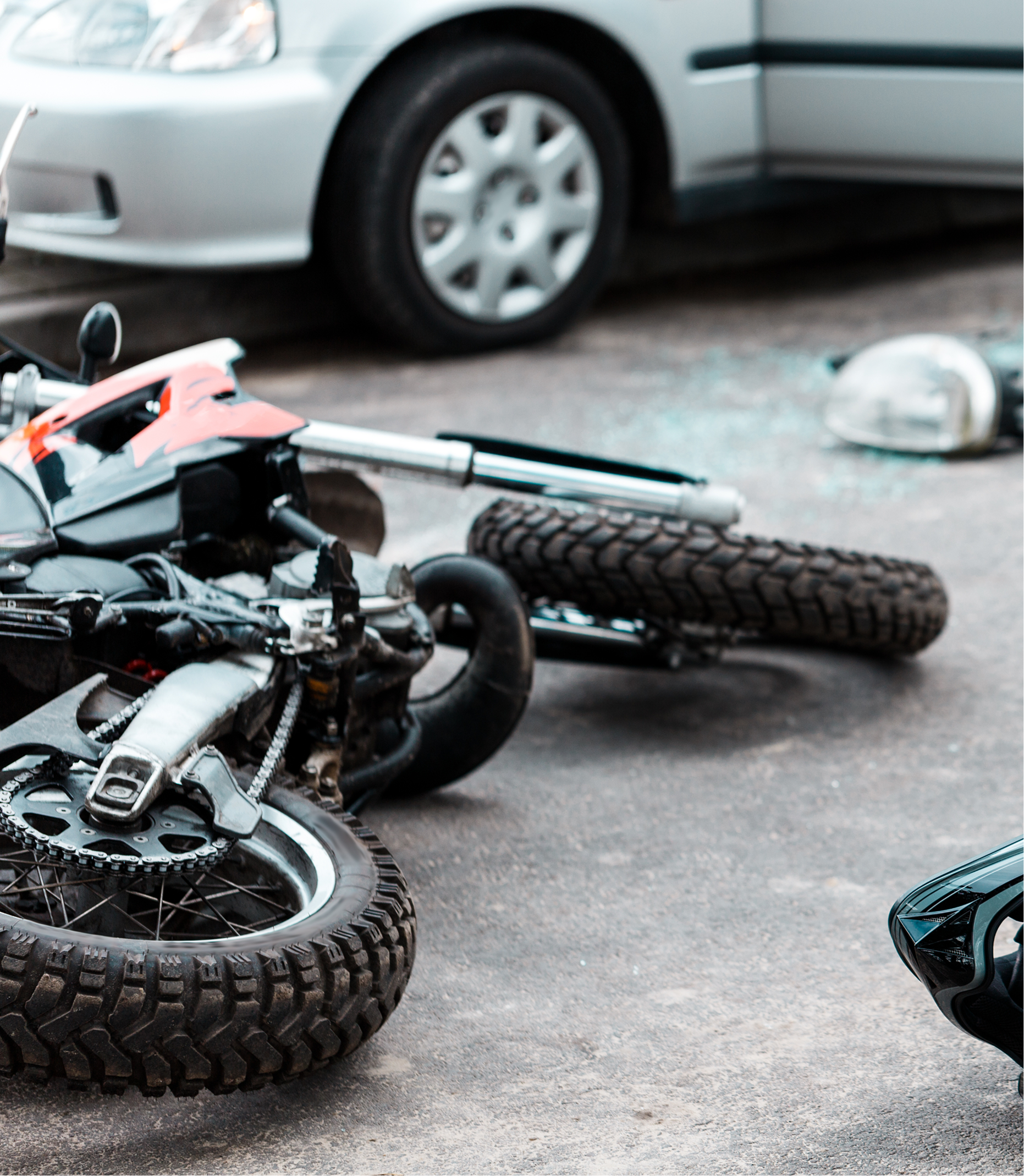Two dirt bikes toppled on pavement beside a parked silver car