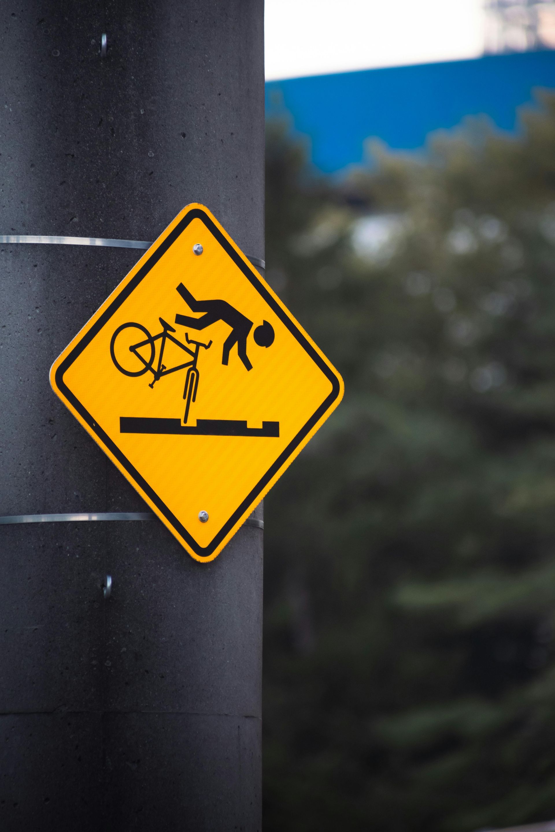 Yellow warning sign showing a cyclist falling from a bike on a black pole outdoors
