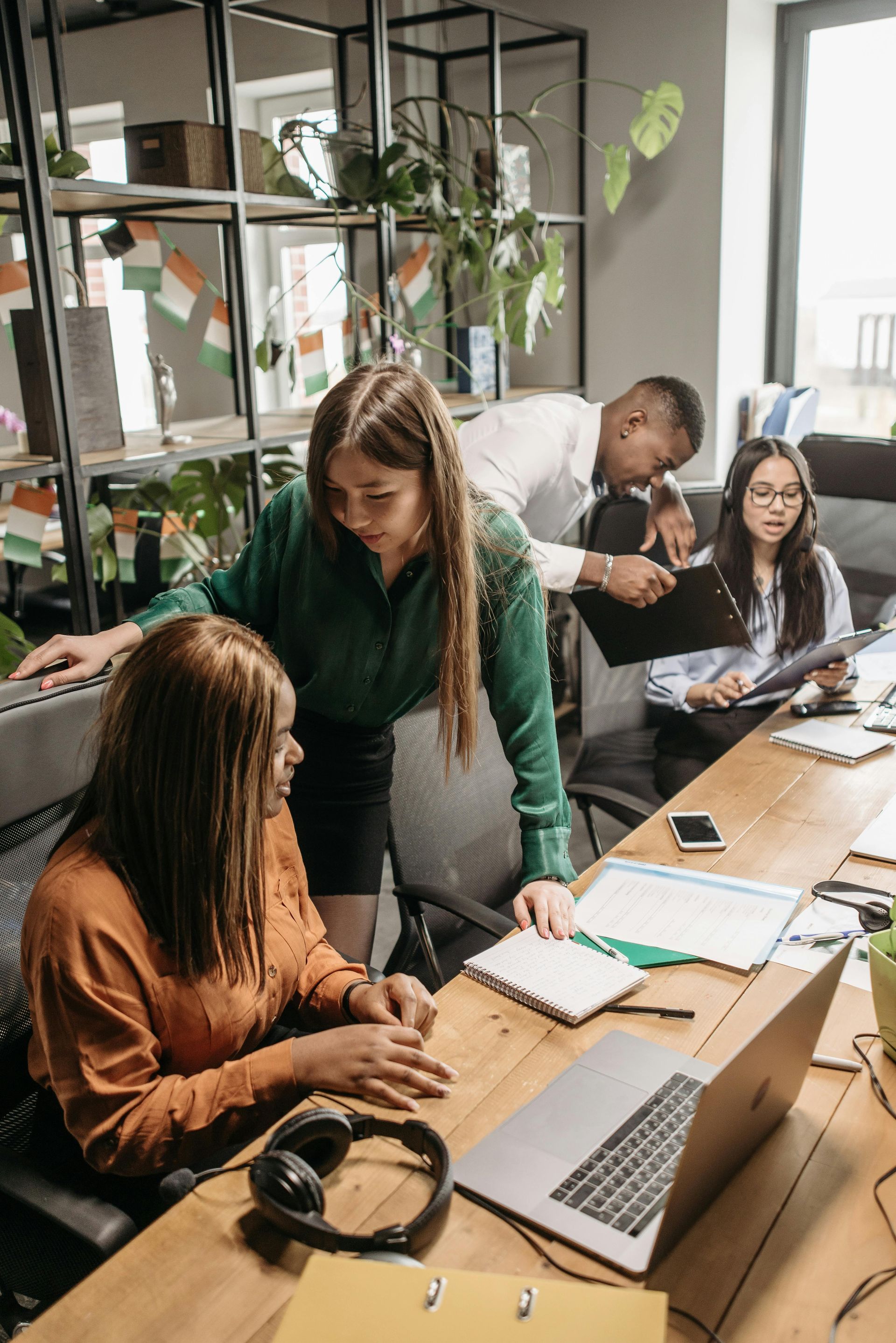 Office team collaborating around a laptop at a wooden table near a bright window