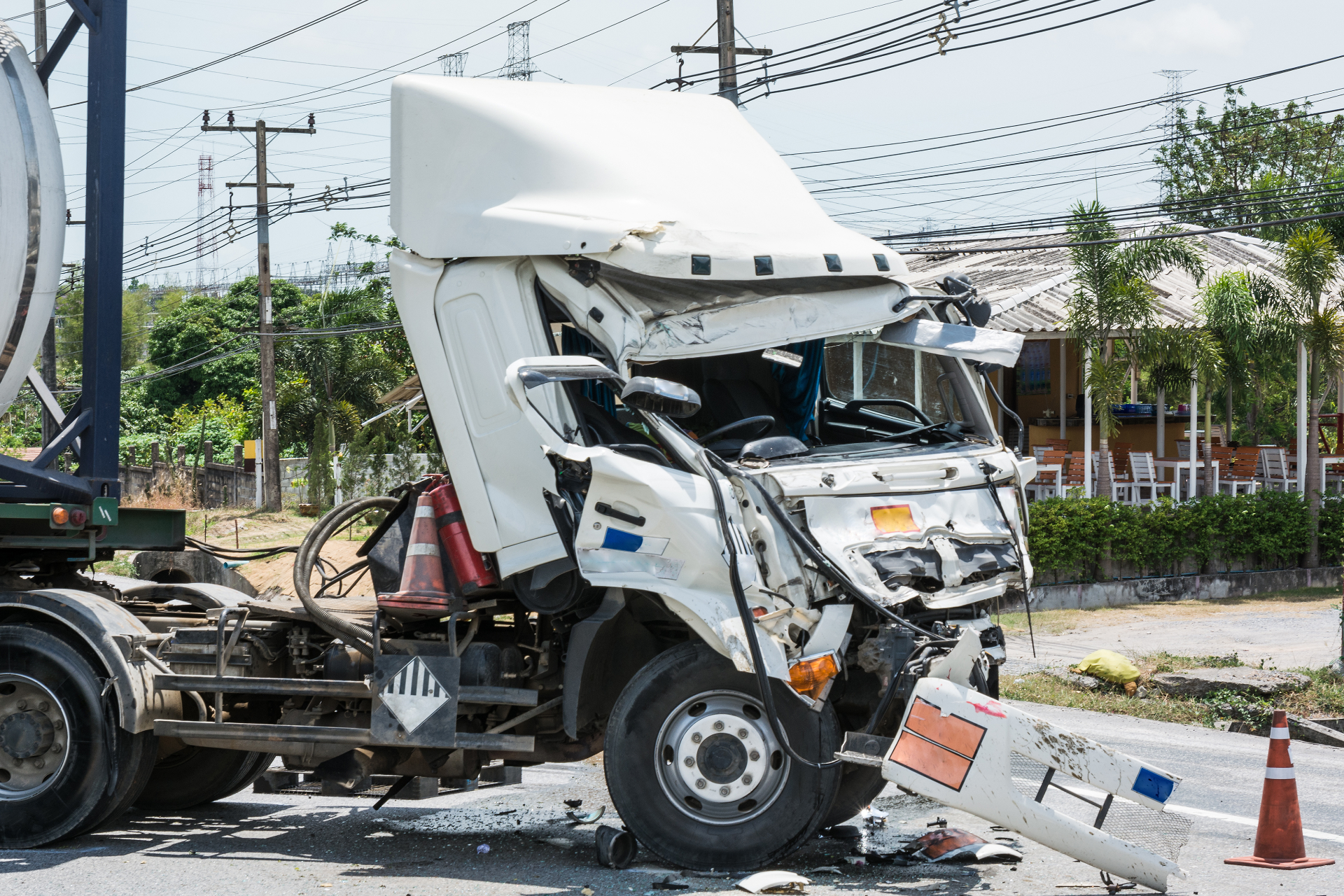 Damaged white semi-truck cab crashed on roadside near cones and debris