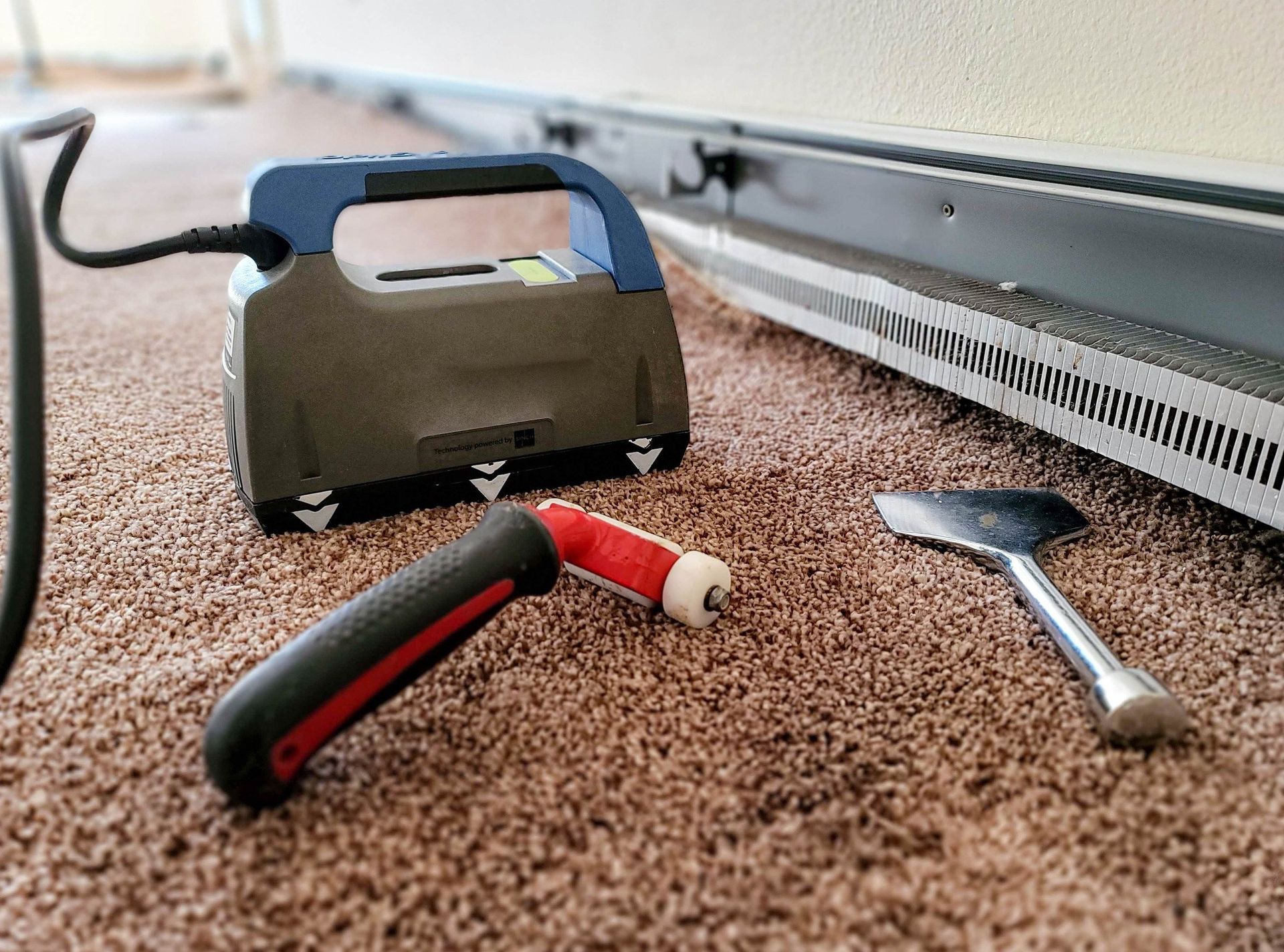 A carpet cleaner is sitting on a carpet next to a spatula.
