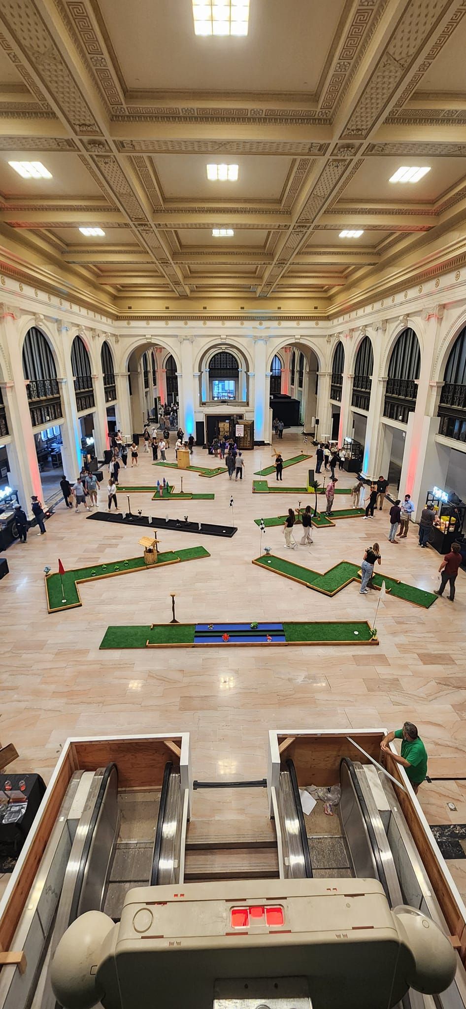 People playing mini golf in a grand hall with marble floors and ornate architecture.
