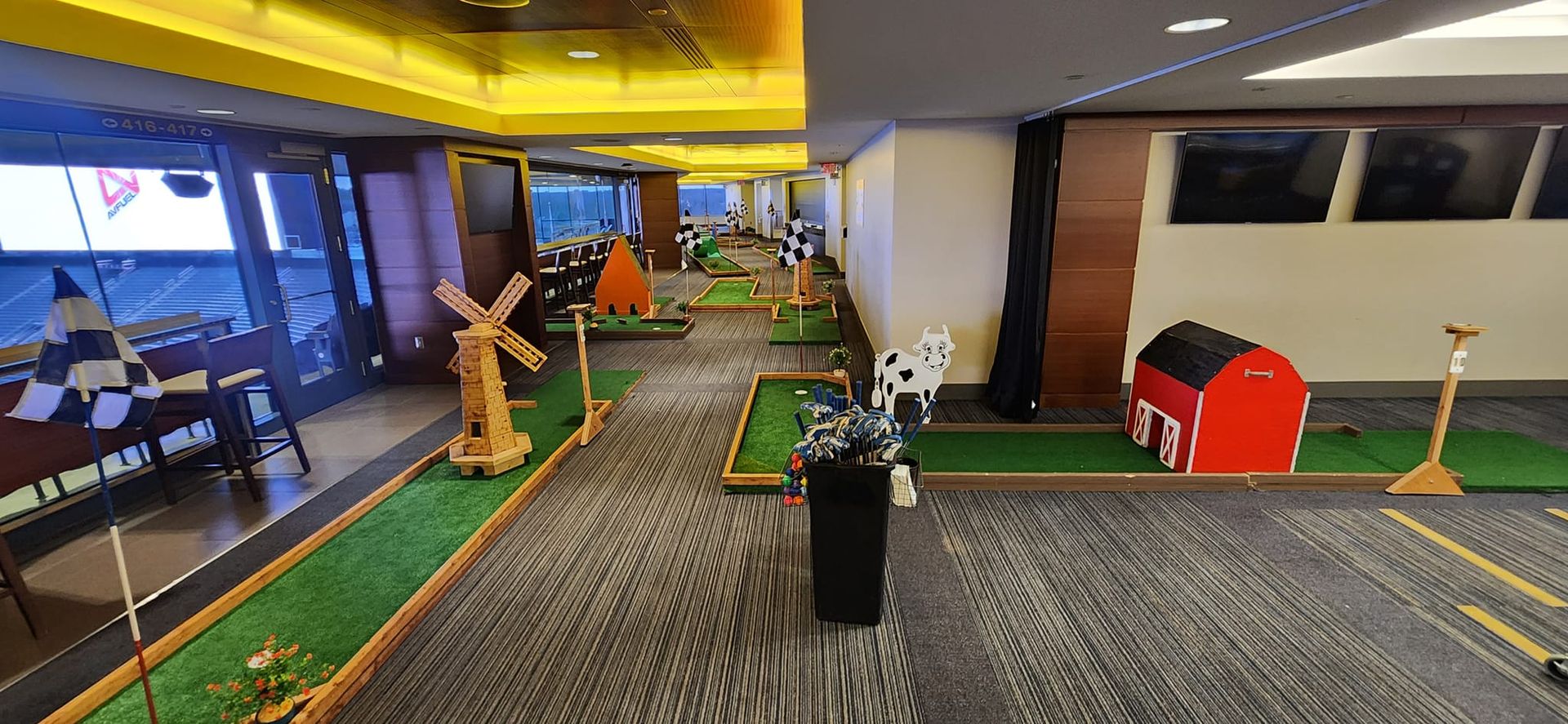 Mini golf course set up indoors with whimsical obstacles like a windmill and a barn.