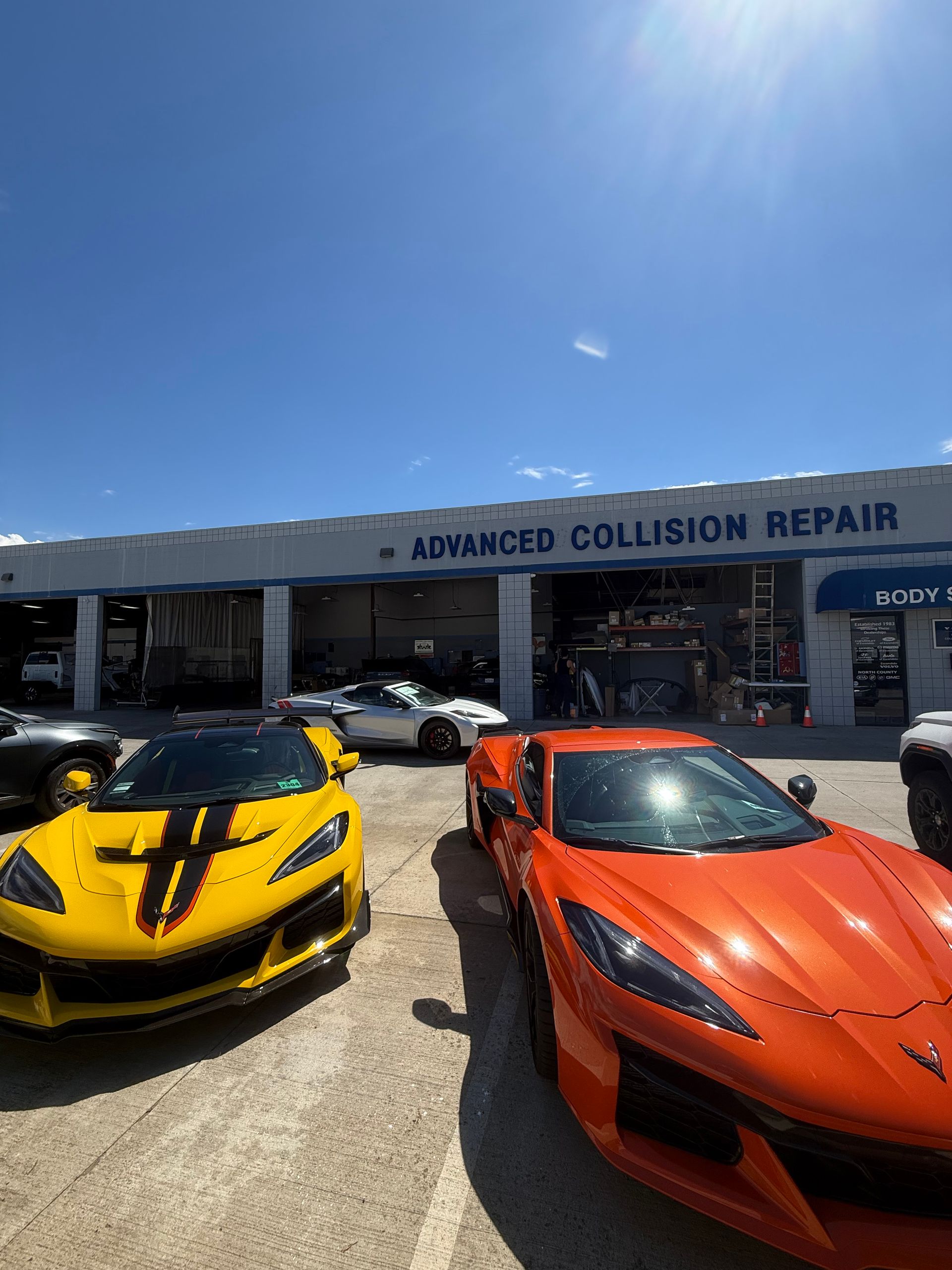 Yellow and orange sports cars parked outside Advanced Collision Repair under a bright blue sky
