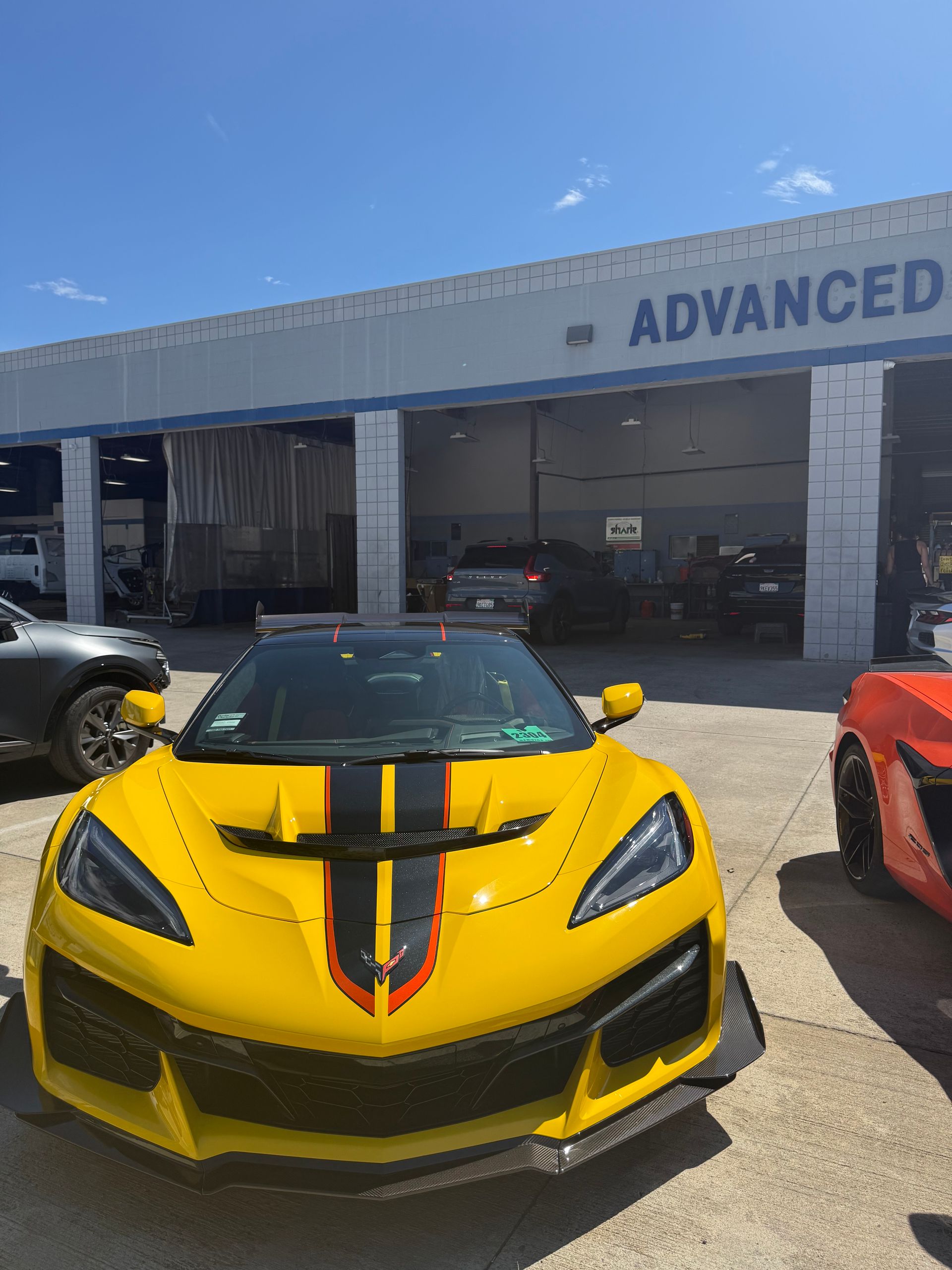 Yellow sports car with black and red racing stripes parked outside an auto shop