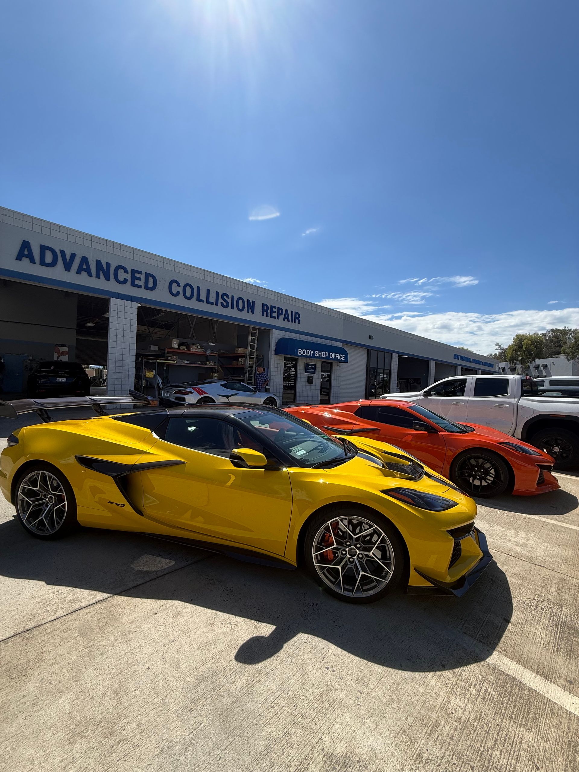 Yellow and orange sports cars parked outside Advanced Collision Center under a bright blue sky