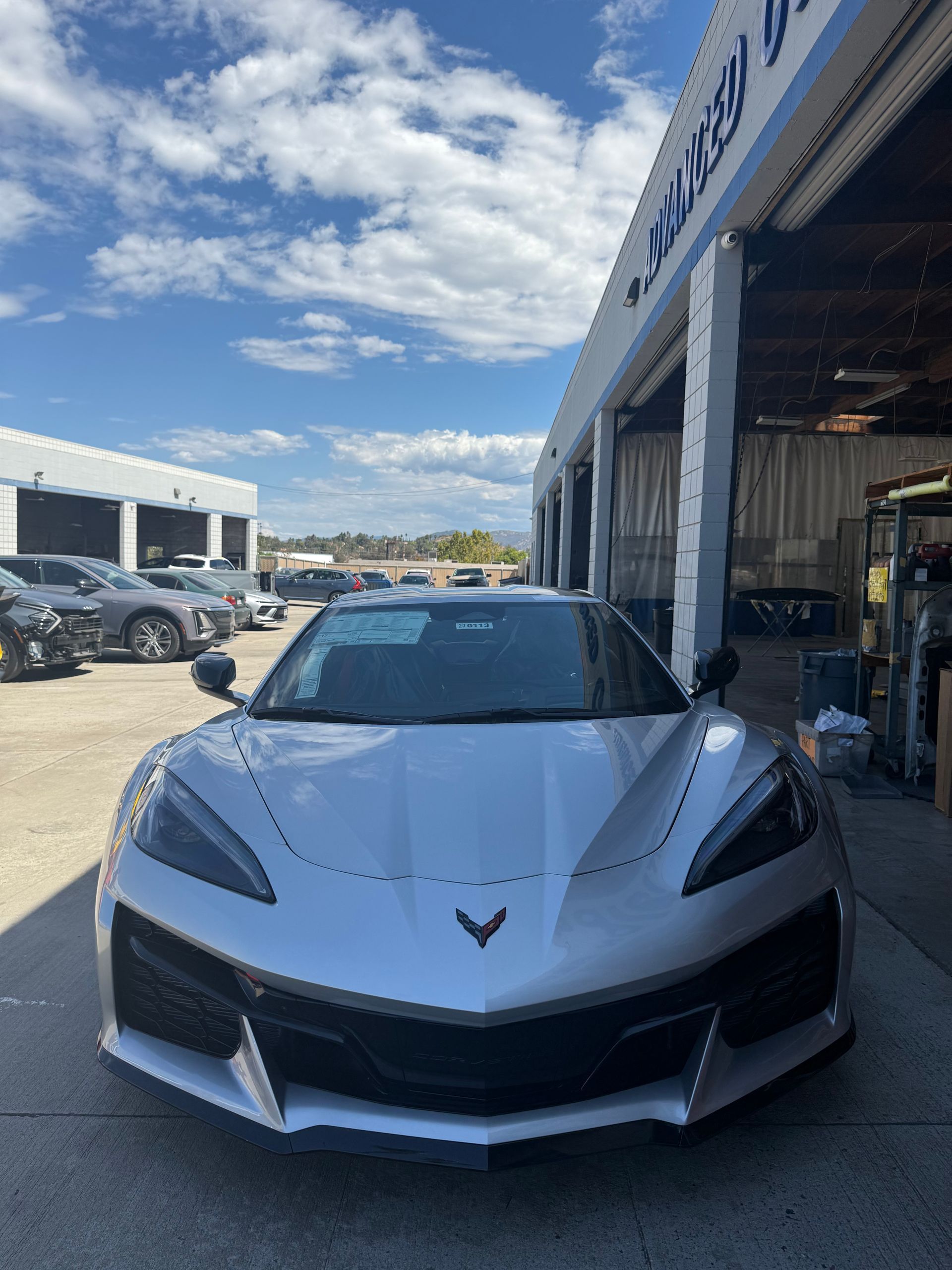 Silver sports car parked outside a dealership garage on a sunny day
