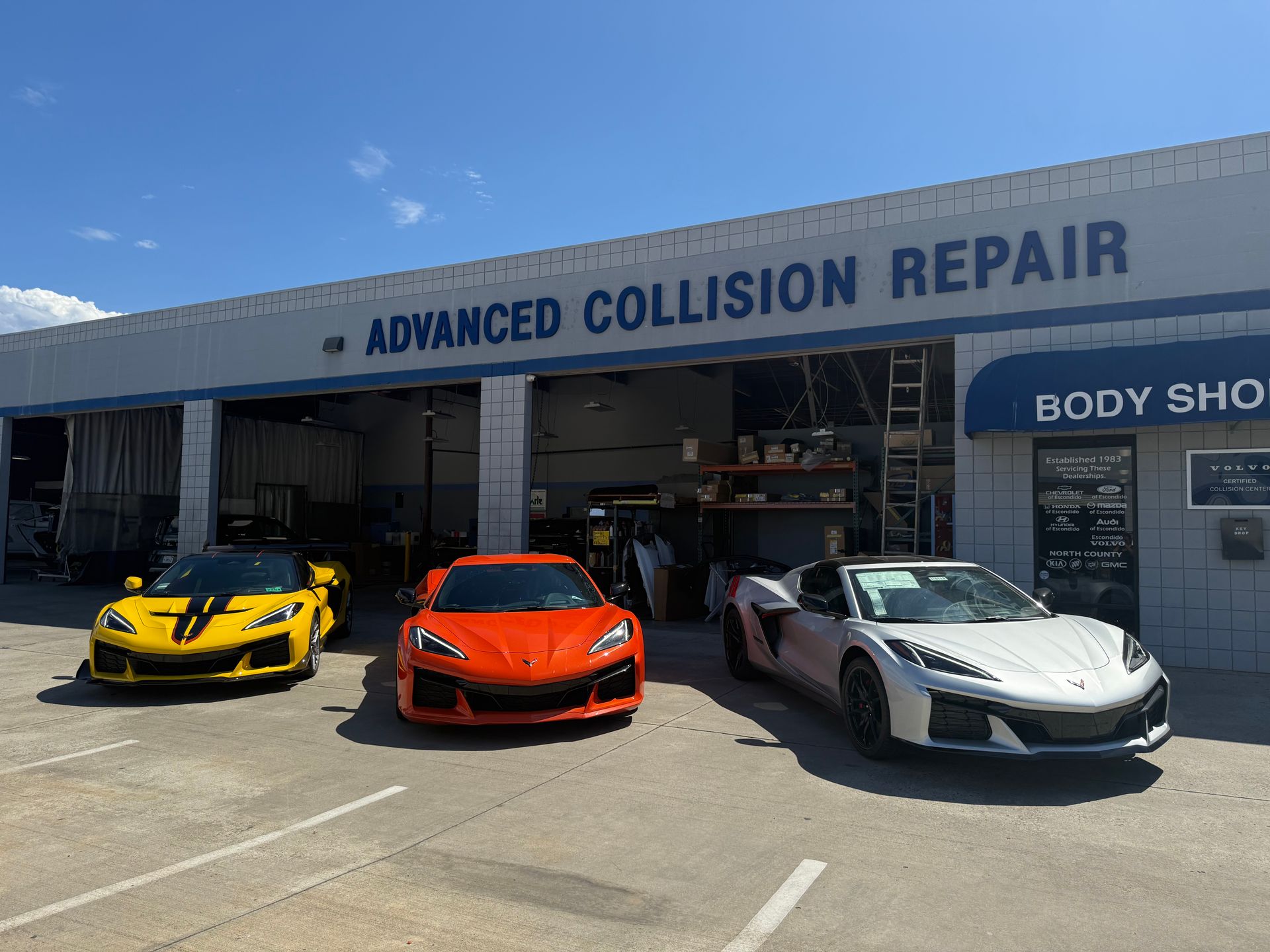 Three sports cars parked outside Advanced Collision Repair body shop on a sunny day